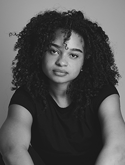 Porträtfoto von Fatima Xavier mit lockigem Haar und ernstem Gesichtsausdruck. Sie trägt ein dunkles T-Shirt und schaut direkt in die Kamera. Das Bild ist in Schwarz-Weiß.