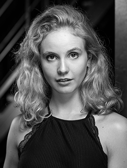 Porträtfoto von Franziska Wagner mit welligem, blondem Haar, die direkt in die Kamera blickt. Sie trägt ein dunkles Oberteil mit Spitzenrand. Das Foto ist in Schwarz-Weiß gehalten.