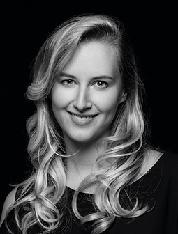 Porträtfoto von Martina Pallinger mit langen, gewellten Haaren, die sie seitlich trägt. Sie lächelt leicht und trägt ein schwarzes Oberteil. Das Bild ist in Schwarz-Weiß.