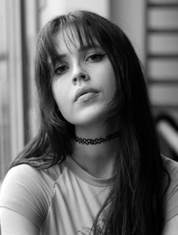 Porträtfoto von Vivian Fuchs mit glatten, dunklen Haaren und Pony, die ein schwarzes Choker-Halsband und ein helles Oberteil trägt. Das Schwarz-Weiß-Bild wirkt künstlerisch.