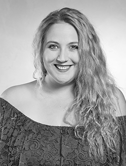 Porträtaufnahme von Alicia Wagner, lächelnd mit welligem, offenem Haar, vor hellem Hintergrund, in Schwarz-Weiß