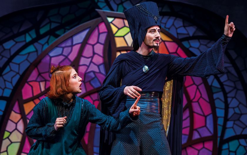 Ein finsterer Zauberer in dunklem Gewand spricht energisch, während eine junge Frau ihn aufmerksam beobachtet.