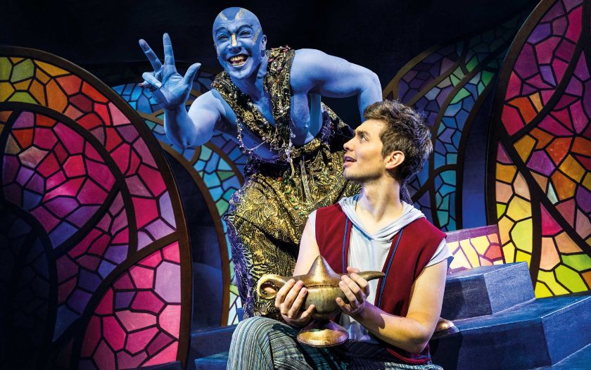 Dschinni erscheint aus der Lampe und begrüßt Aladin mit breitem Grinsen.