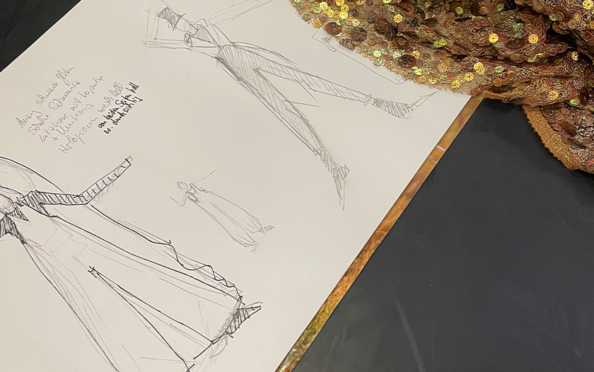 Skizzenblätter mit mehreren Kostümentwürfen und goldenem Paillettengewebe auf dunklem Hintergrund