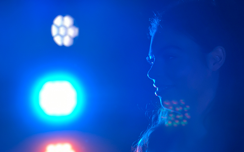 Silhouette einer Frau vor blauem und lilafarbenem Bühnenlicht, unscharf im Gegenlicht