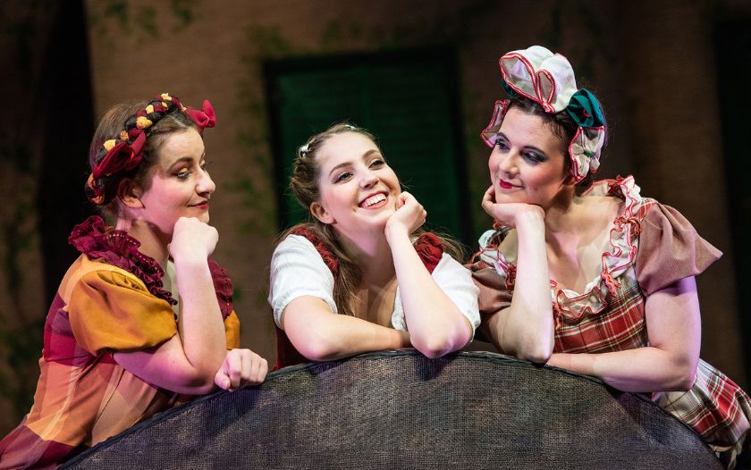 Belle und zwei andere junge Frauen lehnen sich lächelnd über einen Zaun