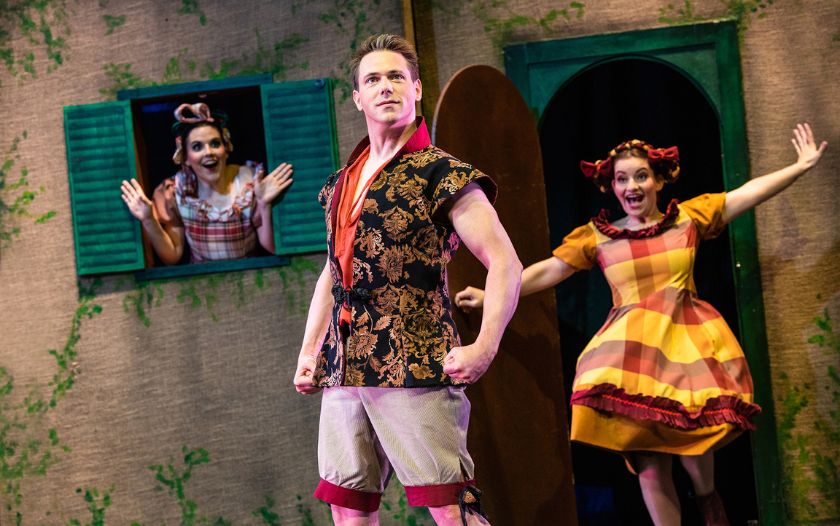 Taureau posiert im Vordergrund, während zwei Frauen aus einem Hausfenster und einer Tür schauen