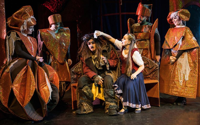 Belle tupft dem verletzten Biest fürsorglich die Stirn, umgeben von Schlossbewohnern