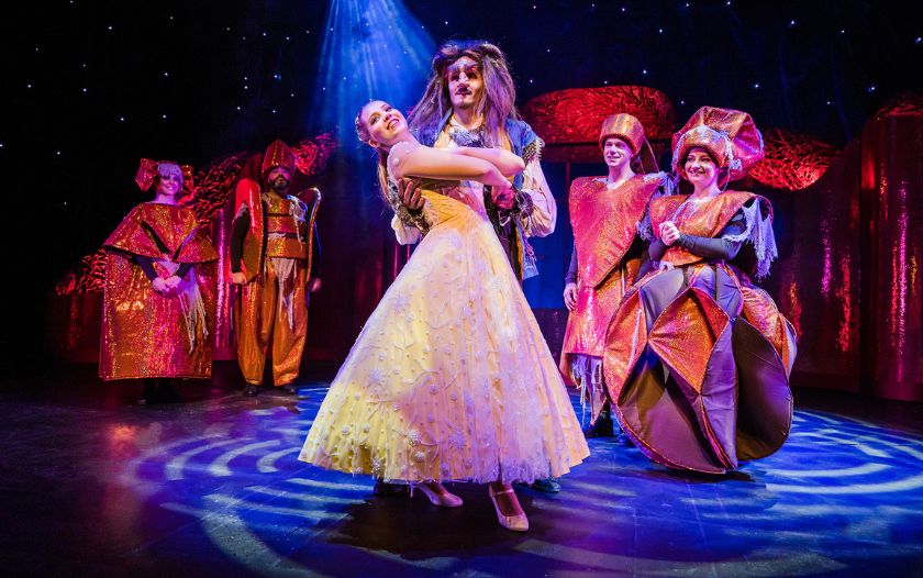 Belle und Biest tanzen in festlicher Atmosphäre umgeben von Schlossbewohnern