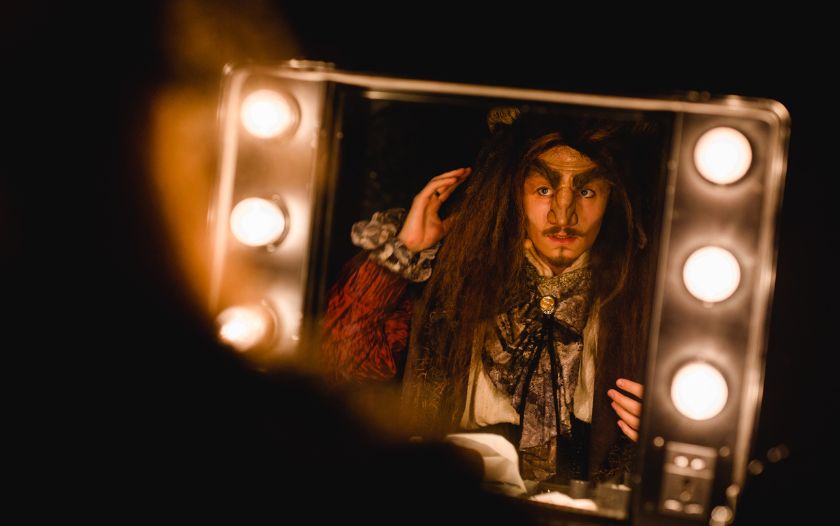 Der Darsteller des Biests schaut sich im Spiegel an, während er seine Maske kontrolliert