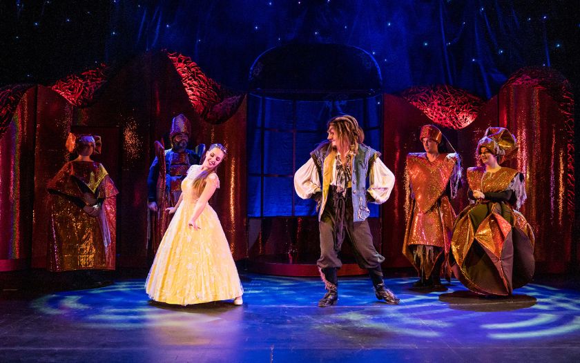 Belle in einem gelben Kleid tanzt mit dem Biest vor den Schlossbewohnern in einer Szene des Musicals „Die Schöne und das Biest“