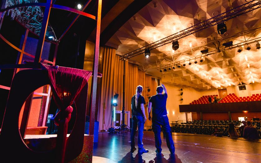 Zwei Techniker stehen auf der Theaterbühne und schauen in den Zuschauerraum