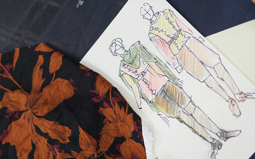 Zwei farbige Modezeichnungen zeigen historische Kostümentwürfe für männliche Figuren von Theater Liberi, daneben liegen passende Stoffproben. Die Skizzen sind mit Buntstift koloriert und durch feine Linien strukturiert.