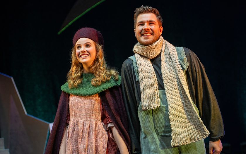 Gerda und Kai lächeln gemeinsam auf der Bühne. Sie tragen warme Kleidung, wie einen Schal und Mütze