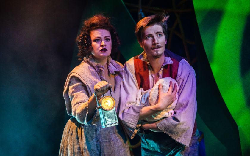 Ein Mann mit einem Baby im Arm und eine Frau mit einer Laterne stehen in einer düsteren Dschungelkulisse und blicken erschrocken nach vorne.