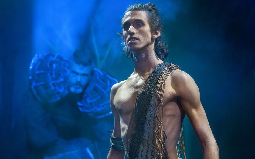 Tarzan steht mit ernstem Blick im Vordergrund der Bühne. Im Hintergrund lauert Bösewicht Olivia Clayton in bedrohlicher Haltung. Die Szene stammt aus dem Musical 'Tarzan – das Musical' von Theater Liberi.