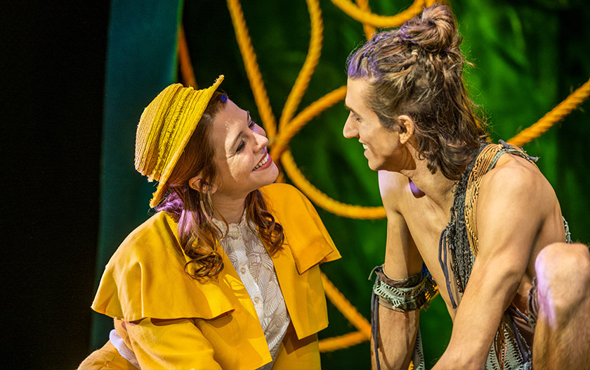  Gespräch	Tarzan mit nacktem Oberkörper und geflochtenem Haar sitzt lächelnd einer Frau im gelben Kostüm gegenüber, beide schauen sich liebevoll an.