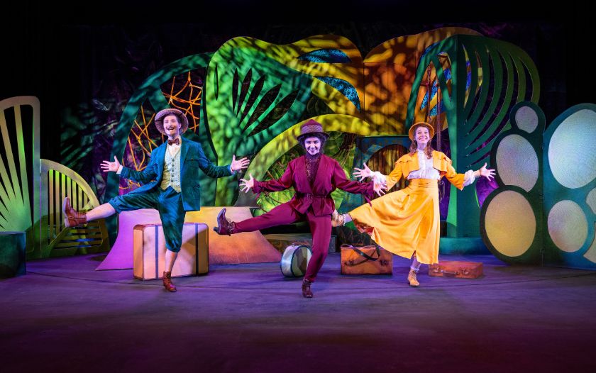 Drei Darsteller:innen in farbenfrohen Kostümen – gelb, rot und türkis – tanzen synchron auf der Bühne vor einer fantasievollen Dschungelkulisse im Musical 'Tarzan – das Musical' von Theater Liberi.