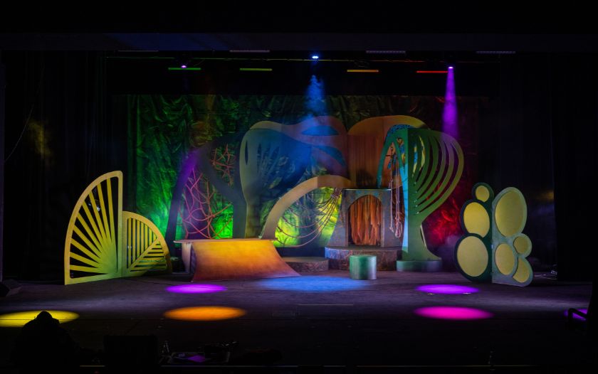 Leere Bühne mit fantasievollen Dschungel-Kulissenteilen, Seilen und bunten Scheinwerferlichtern. Die Bühne ist bereit für eine Szene aus 'Tarzan – das Musical' von Theater Liberi.