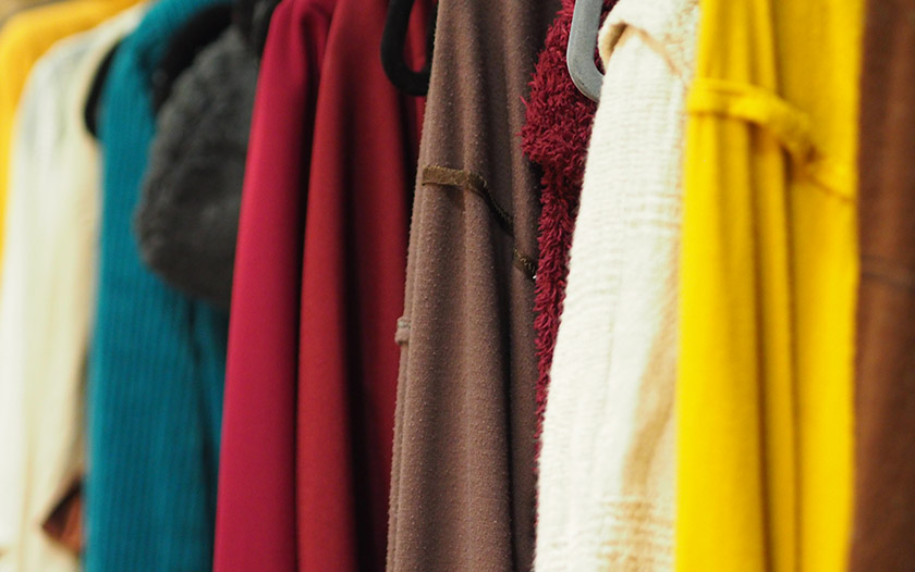 Reihe von farbigen Kostümen in Gelb, Weiß, Braun, Rot, Blau und weiteren Tönen hängt backstage auf einer Kleiderstange.