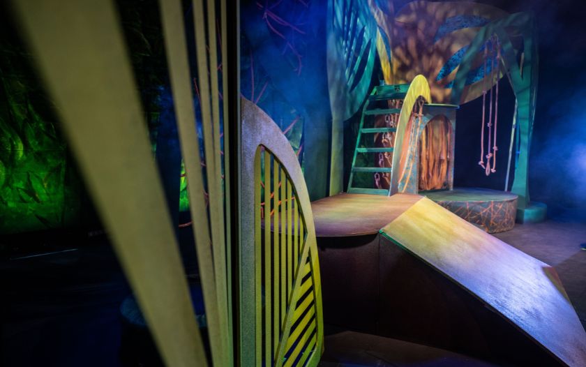 Leere Bühne mit fantasievollen Dschungel-Kulissenteilen, Seilen und bunten Scheinwerferlichtern. Die Bühne ist bereit für eine Szene aus 'Tarzan – das Musical' von Theater Liberi.