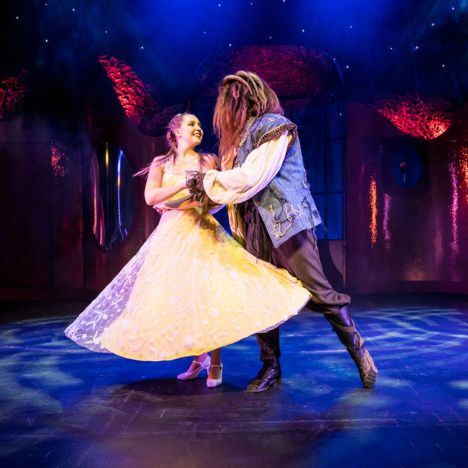 Belle und das Biest tanzen gemeinsam auf der Bühne unter romantischer Beleuchtung.