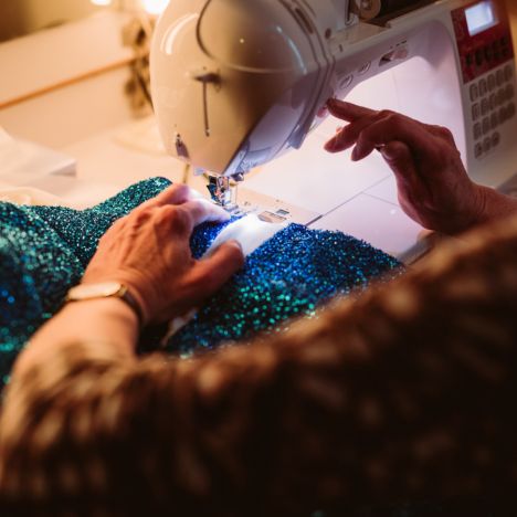 Nahaufnahme einer Nähmaschine, an der eine glitzernde Bühnenrobe genäht wird.