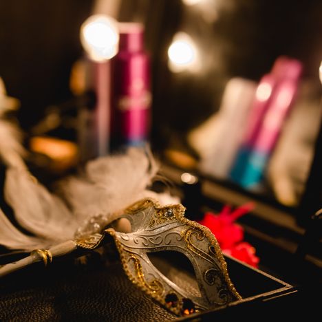 Detailaufnahme eines Schminktischs mit venezianischer Maske, Spiegellichtern und unscharfem Hintergrund.