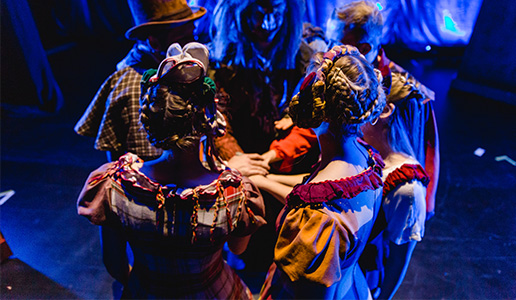 Ensemble in bunten Kostümen steht im Kreis hinter der Bühne mit den Händen übereinander – Moment der Konzentration vor dem Auftritt bei Theater Liberi.