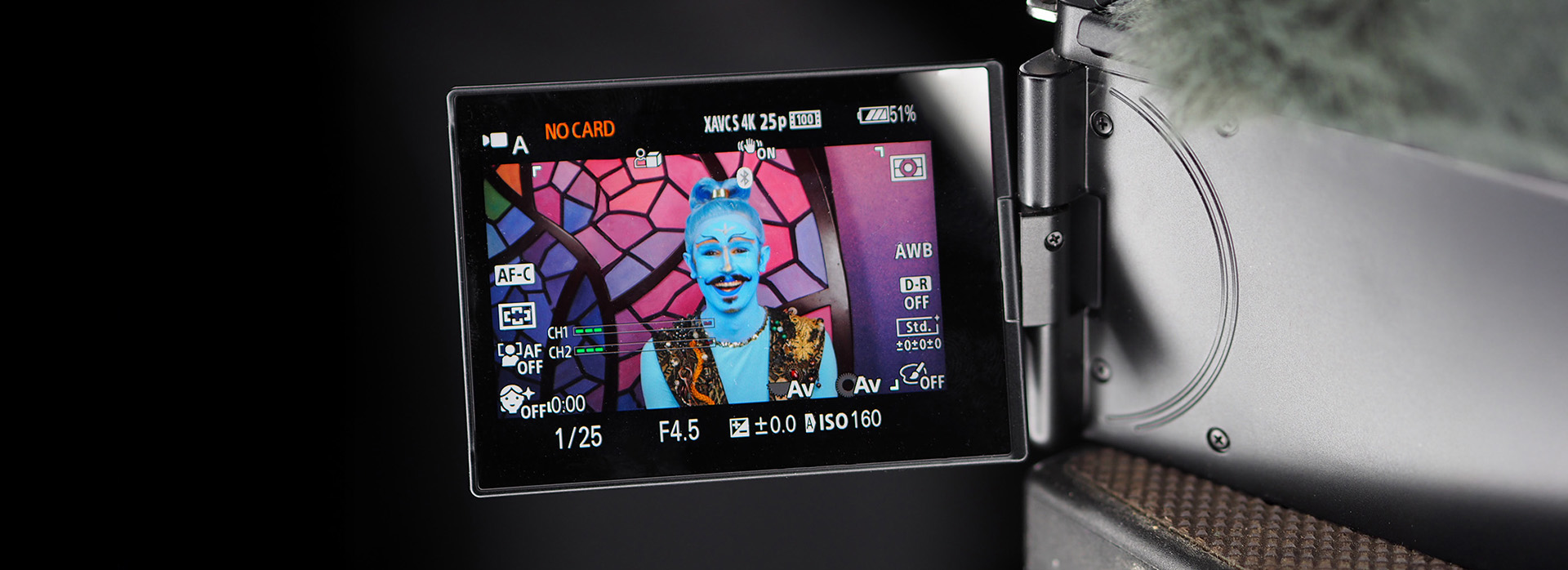 Kameradisplay zeigt fantasievoll geschminkte Bühnenfigur mit blauem Gesicht und orientalischem Kostüm vor buntem Mosaikhintergrund während einer Videoaufnahme.