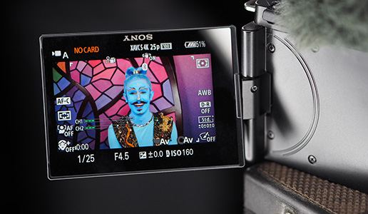 Nahaufnahme des Kameradisplays mit einer fantasievoll geschminkten Person im Bühnenkostüm, aufgenommen bei Videoaufnahmen vor einem farbigen Mosaik-Hintergrund.