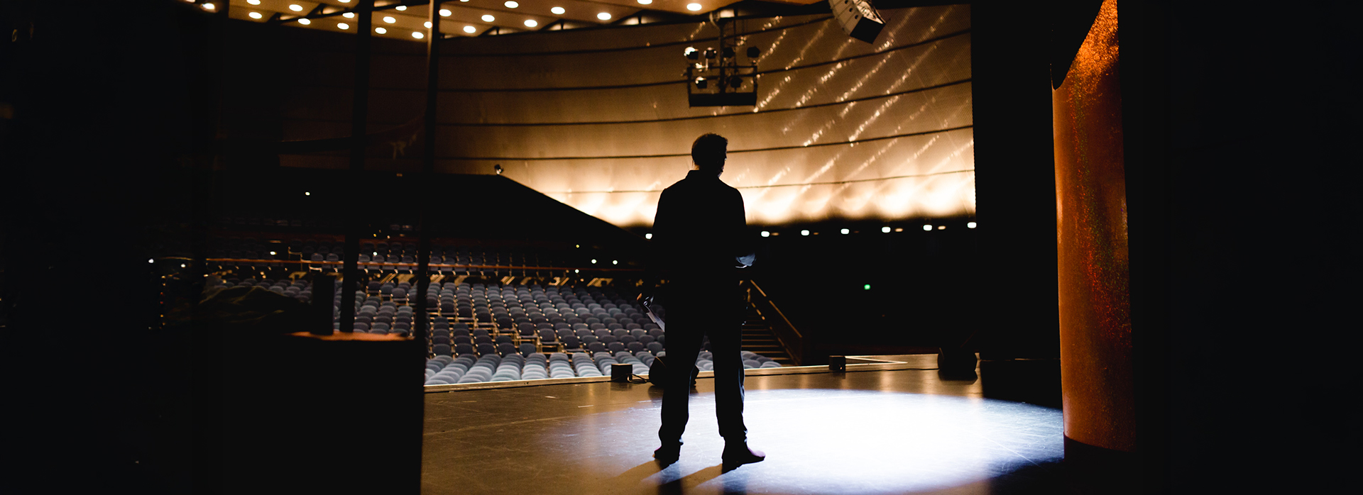 Silhouette eines Darstellers bei der Bühnenprobe im leeren Zuschauerraum – die Bühne ist in stimmungsvolles Licht getaucht.