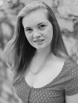 Portraitfoto von Cassandra Schütt, junge Frau mit langen glatten Haaren, die vor einer Natursteinwand posiert, monochrom