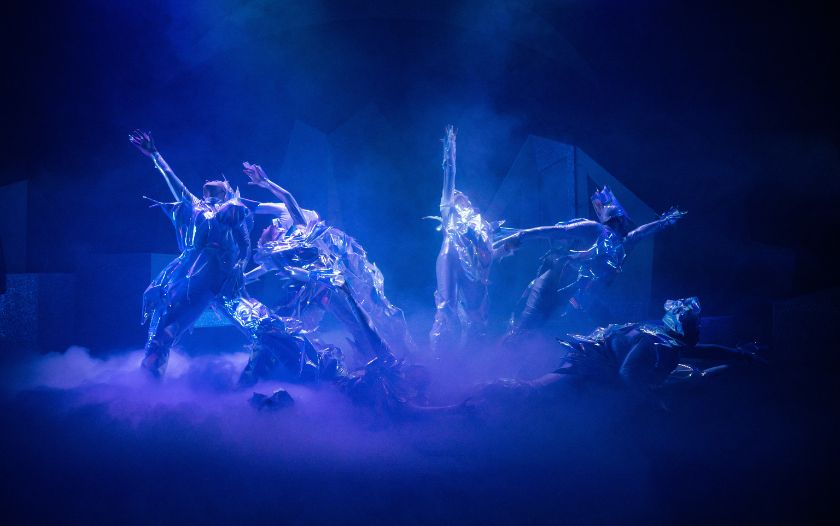 Tänzer in glitzernden Kostümen bei einer eisigen Choreografie im Nebel