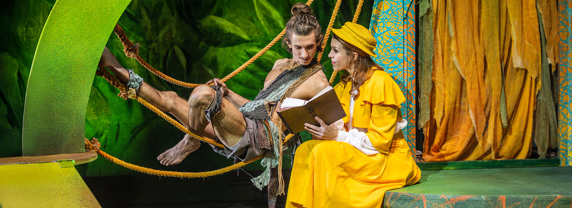 Tarzan liegt in Lianen, während er gemeinsam mit Jane ein Buch liest – Szene aus „Tarzan – das Musical“ von Theater Liberi