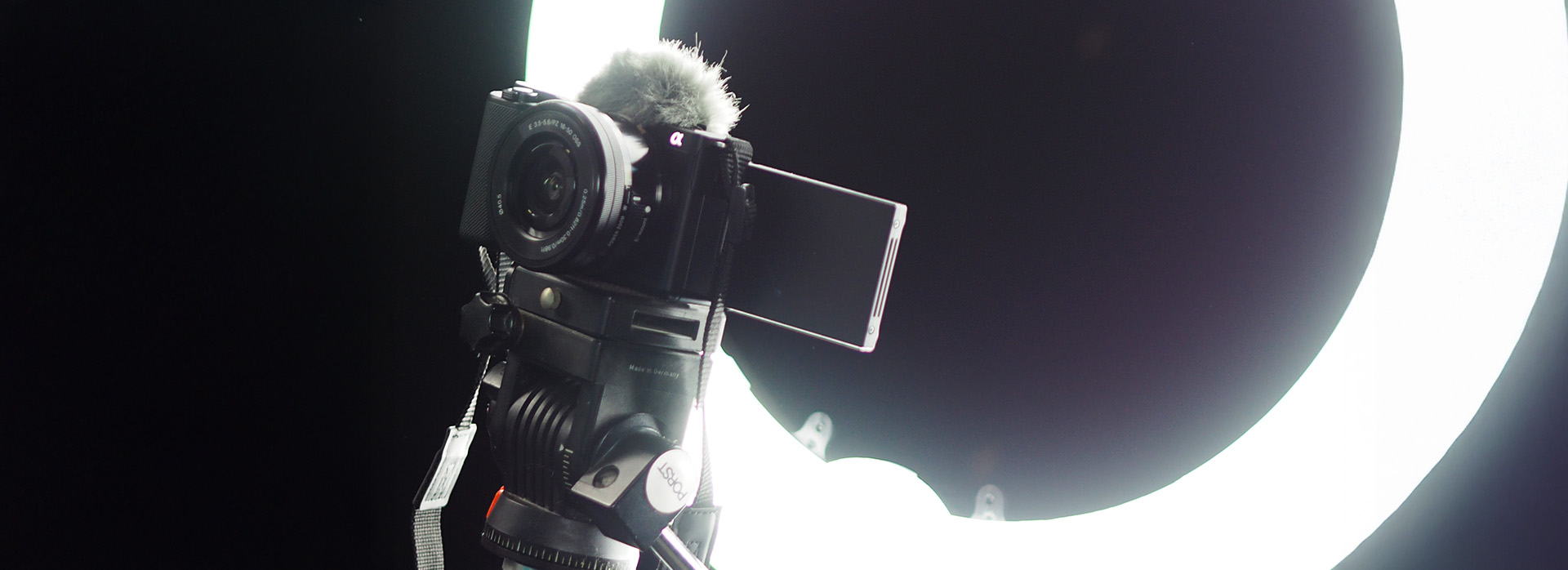 Digitalkamera auf Stativ vor einem hellen Ringlicht in dunkler Studioumgebung, bereit für Videoaufnahmen oder Fotoshootings.