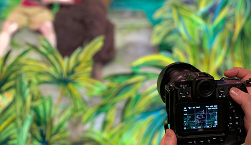 Fotograf hält Kamera auf eine farbenfrohe Bühnenszene mit Dschungelhintergrund gerichtet, im Fokus eine Aufnahme während einer Theateraufführung.