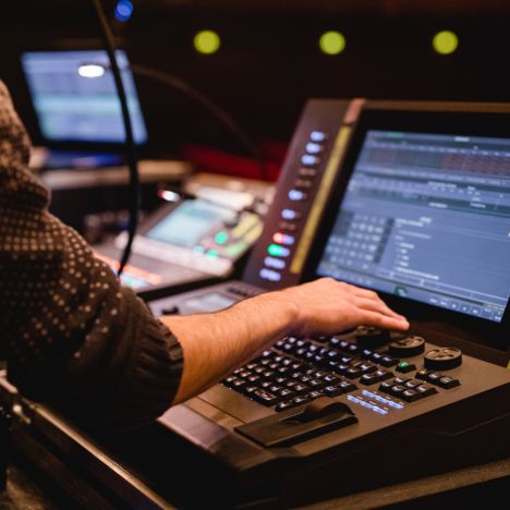 Hand eines Technikers an einem modernen Licht- und Tonpult im Theater mit geöffneten Steuerungsprogrammen.